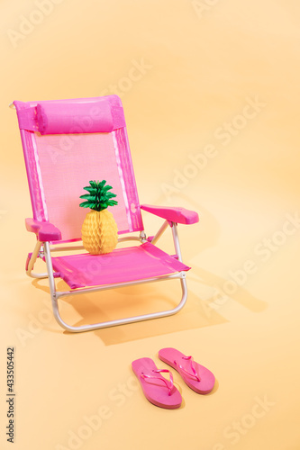 Pink beach chair with a paper pineapple on top and pink flip flops