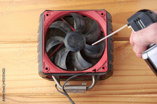 A closeup of a male hand using can of compressed air to blow away dust of big computer fan on wooden table. Computer maintenance.