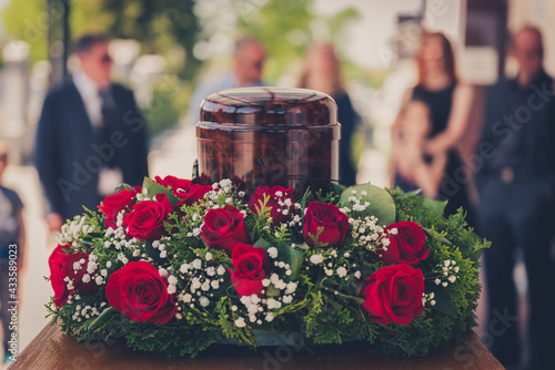 Funerary urn with ashes of dead and flowers at funeral.