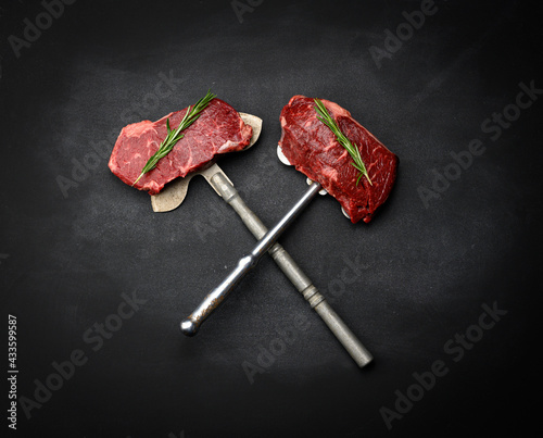 two raw pieces of beef steak lie on an iron knife, black background. Classic steak