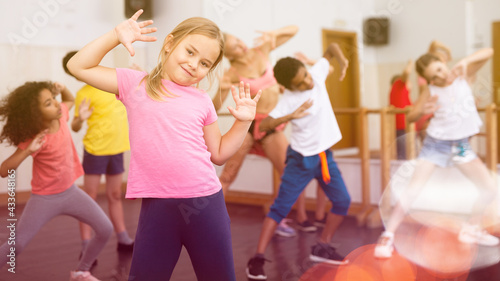 Smiling little girl training movements of vigorous dance with group of tweens in children dance studio..
