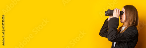 young business woman looking through binoculars on a yellow background. Banner