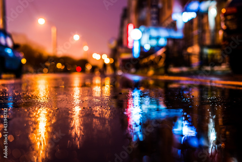 Rainy night in the big city, the street with bright shop windows. Close up view of a puddle on the asphalt level