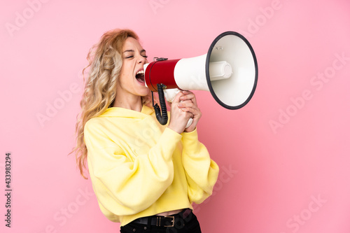 Young blonde woman wearing a sweatshirt isolated on pink background shouting through a megaphone