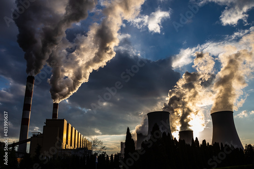 A view of the smoking chimneys of a coal-fired power plant against the backdrop of a dramatic sky with clouds. The photo was taken in natural daylight.