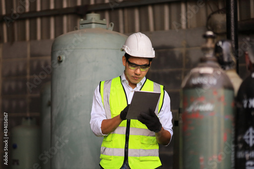 Asian industrial worker using digital tablet to check the coolant system in the factory while standing before liquid nitrogen and argon in compressed container tank for biochemical industry