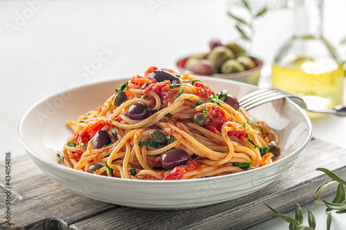 Close up of spaghetti alla puttanesca - italian pasta dish with tomatoes, olives, capers and parsley. Light background.