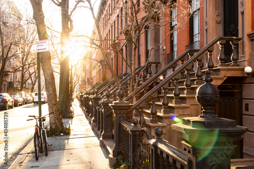 Block of historic brownstone buildings on Charles Street in the West Village neighborhood of New York City with afternoon sunlight shining on the empty sidewalk with no people