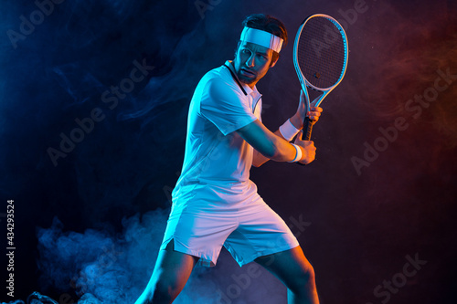 Tennis player with racket in white t-shirt. Man athlete playing on dark background.