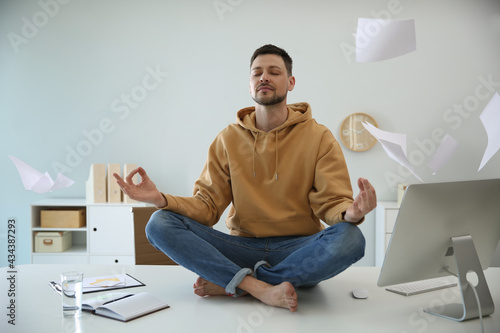 Calm man meditating on office desk in middle of busy work day