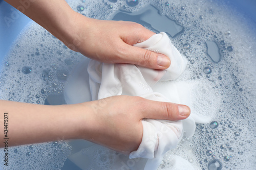 Top view of woman hand washing white clothing in suds, closeup