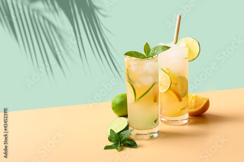 Two summer cold mojito cocktails with orange and lime slices on green and beige background. Refreshing summer beverage with sunny shadow.