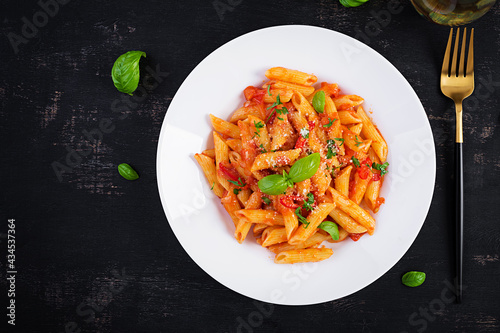 Classic italian pasta penne alla arrabiata with basil and freshly grated parmesan cheese on dark table. Penne pasta with chili sauce arrabbiata. Top view, above, copy space