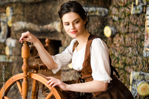 Portrait of Young Lovely Caucasian Brunette Woman Posing With Spinning Wheel in Retro Dress In Rural Environment.