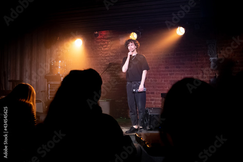 Young Caucasian male comedian performing his stand-up monologue on a stage of a small venue