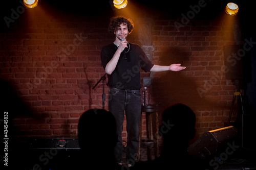 Young Caucasian male comedian performing his stand-up monologue on a stage of a small venue