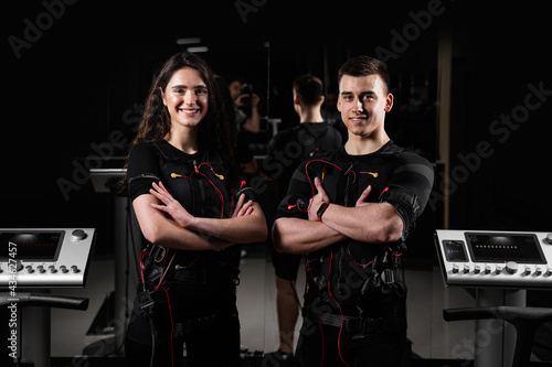 man and a woman in an EMS vest are standing side by side and smiling. 2 trainers in gym.