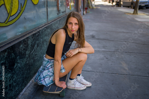 Young Woman Seated With Skateboard on the Sidewalk in a Downtown Area