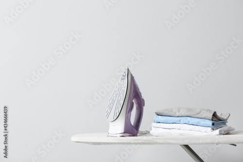 Board with electric iron and clothes on light background