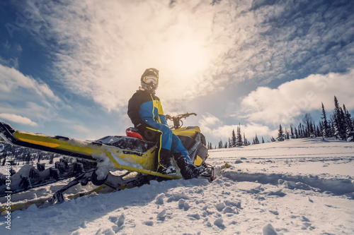 Snowmobile female rider riding on beautiful mountain slope