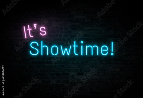 Illuminated and glowing pink and blue "It's Showtime!" neon sign on dark brick wall.