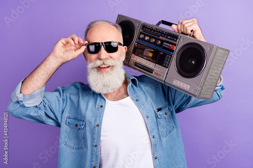 Photo of senior man happy positive smile listen music boombox hipster hand touch sunglass isolated over violet color background