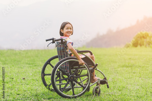 Happy disabled handicapped child sitting in wheelchair on mountain meadow park in sunny day.. International Disability Day.