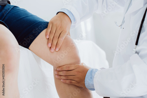 Doctor physiotherapist working examining treating injured knee of patient, his using the handle to the patient knee to check for pain.