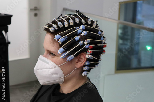 young woman, girl is getting perm, hair curlers on head at hairdressers salon, wearing mask because of corona virus