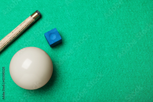 White billiard ball, chalk and cue on green table, flat lay. Space for text