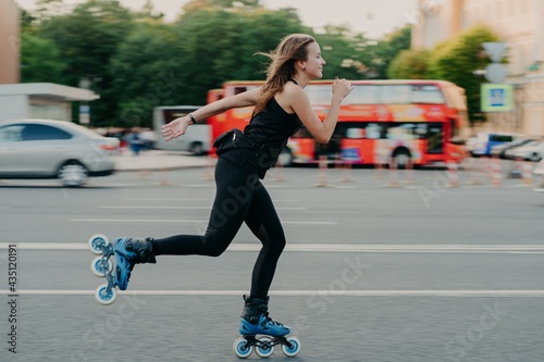 Young fit woman on roller skates with wheels rollerblades during summer day on busy road with transport leads active lifestyle wears black sportsclothes breathes fresh air. Movement concept.