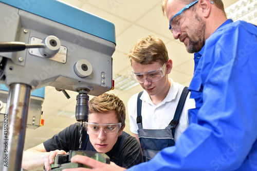 trainer and apprentice in technical vocational training at a drilling machine