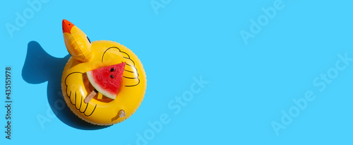 Watermelon slice popsicle on inflatable of yellow duck on blue background. Summer background concept