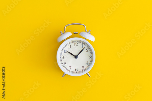 White antique alarm clock on yellow background. Flat lay composition. Top view.