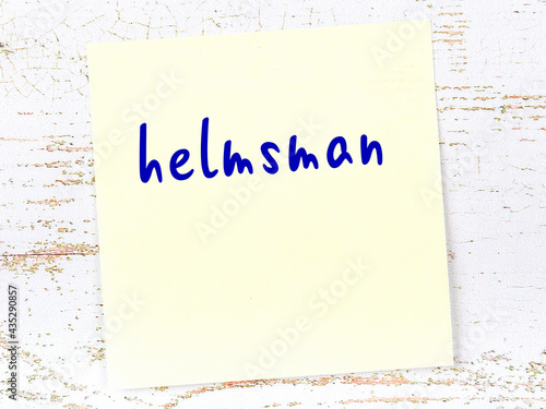 Yellow sticky note on wooden wall with handwritten word helmsman