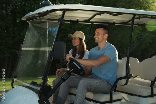 Happy couple driving golf cart in park