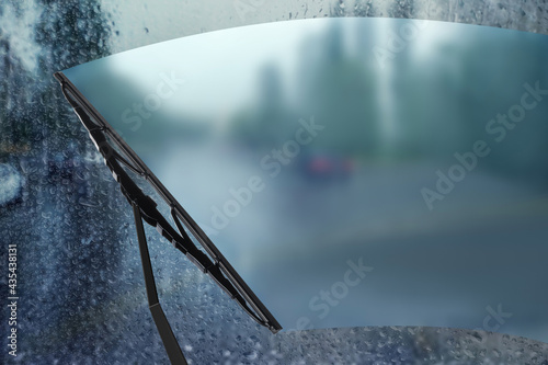 Car windshield wiper cleaning water drops from glass while driving