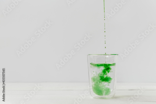 Drops of liquid chlorophyll falling down in a glass cup with water. Light white background with copy space