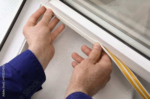 Worker putting rubber draught strip onto window indoors, closeup