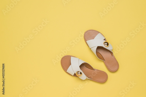 Top view of yellow leather sandals on a yellow background.