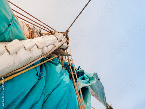 A fragment of a white wooden mast and a turquoise sail of a felucca boat. Bottom view, against the background of the sky.