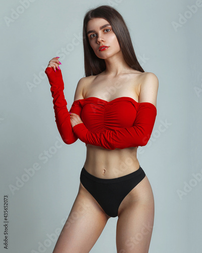 Young woman posing in a red top shirt and black panties, on gray background in studio, copy space. Seductive woman perfect body. Sexy fashion model wear black underwear.