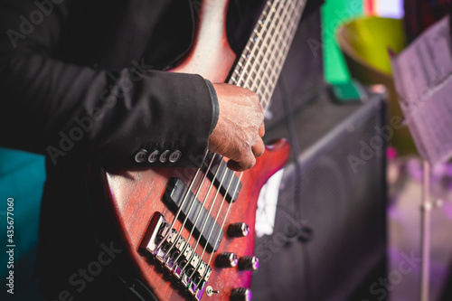 Concert view of an african-american musician with electric bass guitar player during band performing rock music, bassist player on stage