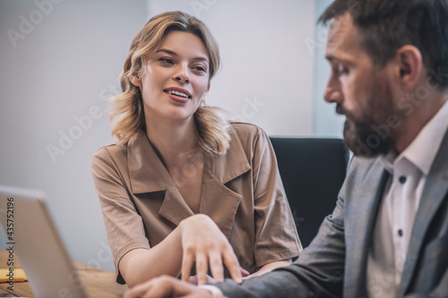 Cheerful young woman touching hand of serious male colleague