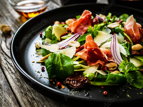 Tasty salad - ham, parmesan and fresh vegetables on wooden background 