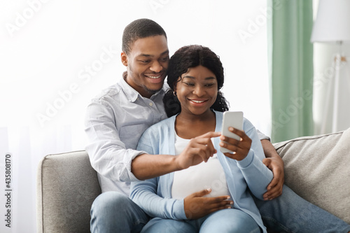 Loving black expecting parents shopping online, using smartphone