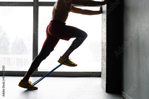 Young shirtless sportsman doing exercise with expander stretch tape