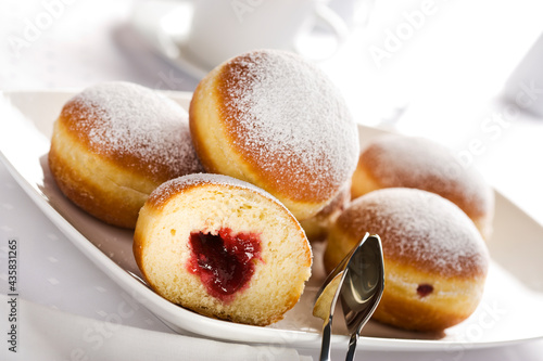 Bismarck doughnuts filled with jam and decorated with confectioner's sugar on a platter with pastry tongs