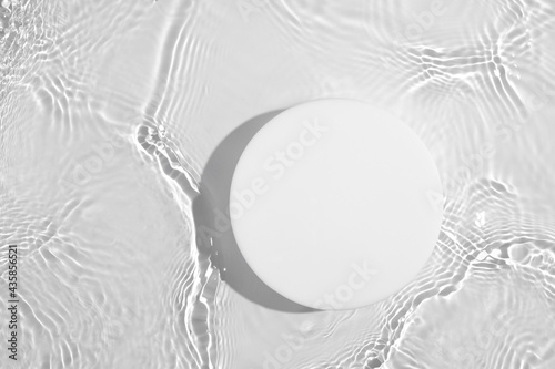 Empty white circle podium on transparent clear calm water texture with splashes and waves in sunlight. Abstract nature background for product presentation. Flat lay cosmetic mockup, copy space.