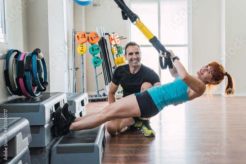 Personal trainer next to a girl exercising with a trx indoors
